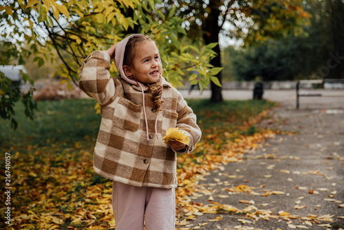 Little girl enjoying an autumn day with fallen leaves in the park