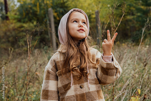 Obraz na płótnie Little girl in brown plaid coat with peace gesture in autumn forest