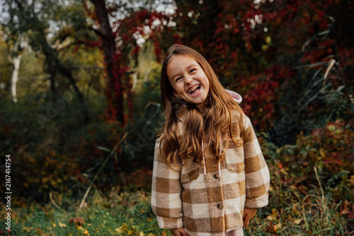 Joyful child enjoying autumn in a plaid coat amidst colorful foliage.