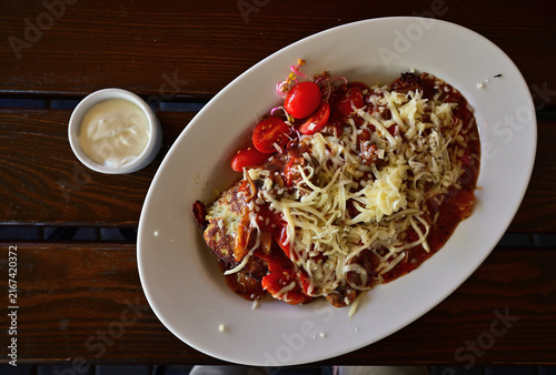 Obraz na plátne Hungarian potato pancake with tomato sauce, melted cheese and sour cream on a white plate served with garlic sauce
