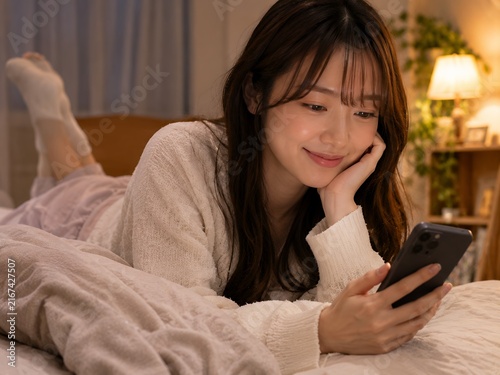 Young japanese woman relaxing in bed and using smartphone at night