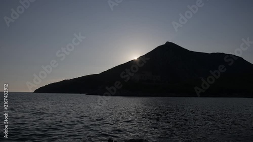 Sun setting over the silhouette of a high hill above the sea. Beautiful sunset over the ocean with mountain silhouettes.