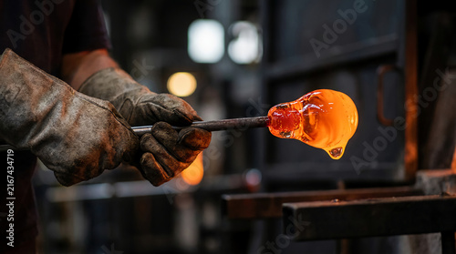 A glassblower shapes molten glass with protective gloves in a workshop, showcasing the craft of glassblowing.