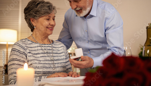 Elderly couple celebrating romance as man presents jewelry box to smiling woman