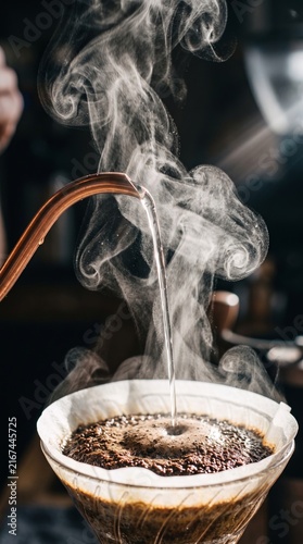 Pouring hot water from kettle onto ground coffee in dripper with rising steam during pour over brew