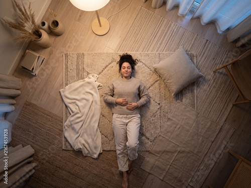 Top view of a serene young woman lying on a cozy rug at home, relaxing and practicing mindfulness in a warm room