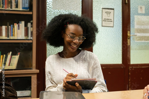 Obraz na płótnie Young woman with afro hair and glasses writing on tablet, laughing during study