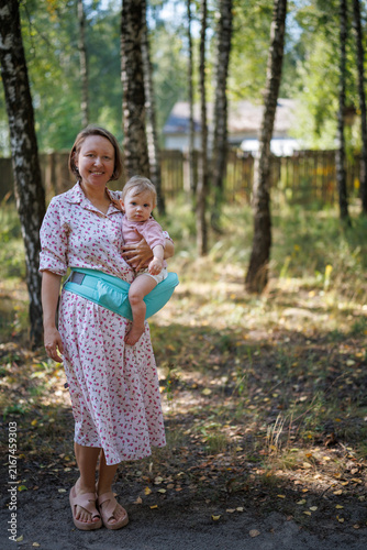 A smiling woman carrying a baby in a turquoise hip seat in a birch forest