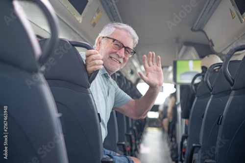 Foto Smiling senior man riding public transit, happily waving hello from his seat whi