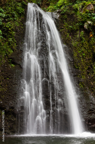 Tall waterfall cascades into pool, lush green forest surrounds. Salto do Prego, Sao Miguel, Azores, Portugal. Natural water flow in scenic landscape.