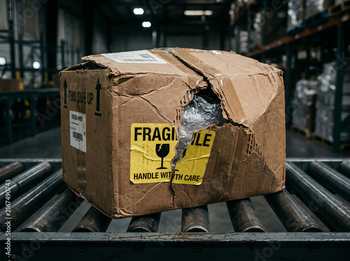 Damaged Cardboard Box with Fragile Sticker Moving on Warehouse Conveyor Belt Line Concept for Logistics Shipping Mishap and Parcel Handling