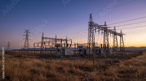 Electrical power substation with transmission towers standing in a dry grass field at dusk