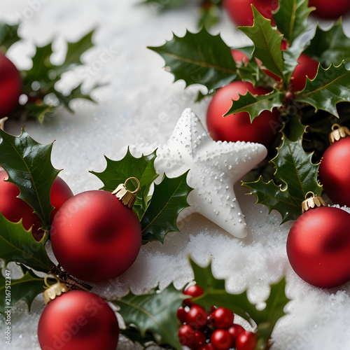 Red Christmas ornament and holly shrub berries and a white star on a snowy surface