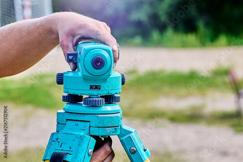 Surveyor steadies optical instrument by hand while setting tripod mounted level for accurate construction layout and land measurement tasks.