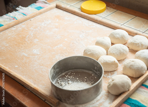 Obraz na plátne Raw dough balls on a floured wooden board beside a metal sifter and rolling pin,