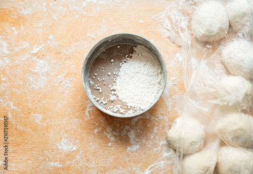Foto Raw dough balls on a floured wooden board beside a metal sifter and rolling pin,