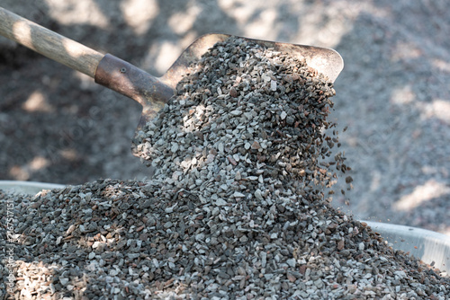 Shovel pouring crushed stone into a wheelbarrow. The process of moving small gravel with a shovel, symbolizing construction work, effort, and material preparation