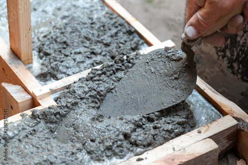 Builder working with concrete in wooden formwork. Close-up of a trowel in fresh concrete mortar inside formwork, symbolizing the foundation construction process