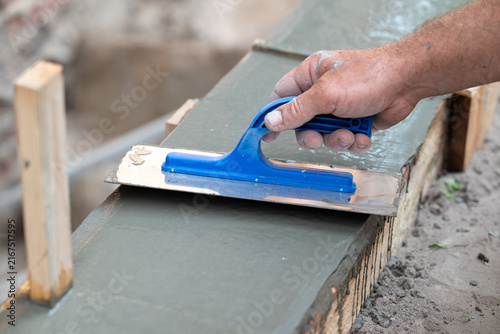 Builder smoothing concrete surface with a float. A worker's hand with a trowel smooths fresh cement mortar on a foundation, symbolizing quality and the final stage