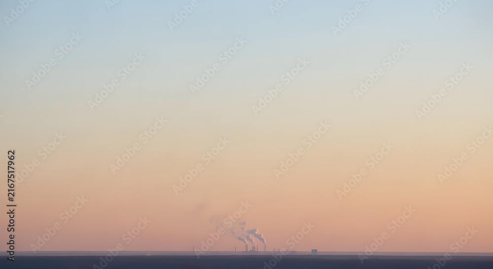 Fototapeta premium Distant industrial smokestacks emitting power plant emissions into a clear soft pastel horizon sky during early morning or sunset