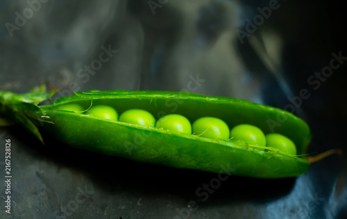 Close-up, macro shot of an open green pea pod on a dark background.