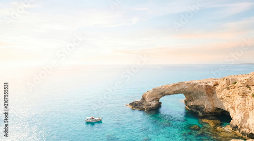 Natural coastal stone bridge and small boat on the bright turquoise Cyprus sea
