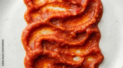 Thick tomato sauce swirls on white plate for cooking.