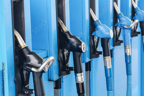 Fuel pump nozzles at station. Black and blue dispenser handles. Diesel and gasoline refueling equipment. Petroleum retail infrastructure for vehicles. Fuel sales form commercial energy background.