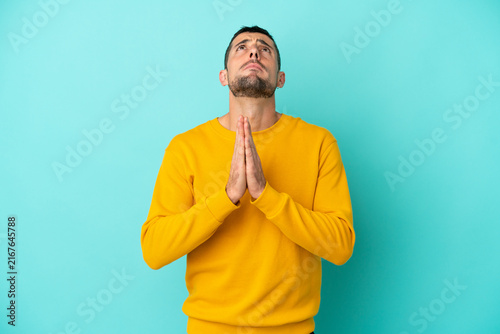 Konstfotografi Young handsome caucasian man isolated on blue background keeps palm together