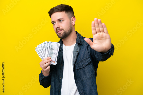 Фотография Young caucasian man taking a lot of money  isolated on yellow background making