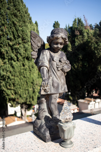 Obraz na płótnie Antica statua di angelo custode con ali e fiori in un cimitero storico, scultura
