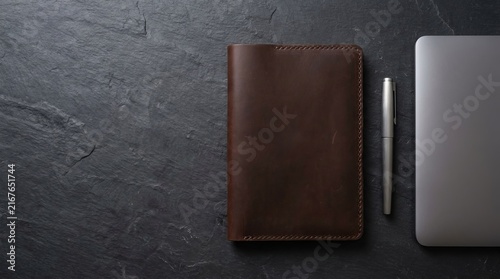Brown leather notebook with pen and laptop on dark surface