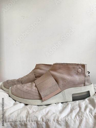 Beige High-Top Canvas Sneakers Viewed from the Back on White Surface. Pair of Blush Pink Sneakers on White Surface. Close-up of Textured Fabric and Leather Material.
