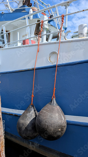 Foto Two black boat fenders hanging from orange ropes.