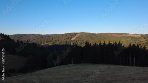 Peaceful aerial drone view over lush green forests and rural countryside on a clear summer morning, with scattered houses, winding roads and natural landscape.