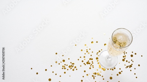 A glass of champagne with golden confetti scattered on a white background