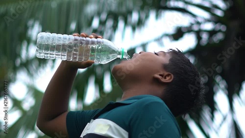 Young Indian Boy Drinking Water From Plastic Bottle Outdoors. Thirsty Rural Indian Kid Drinking Pure Mineral Water Bottle.