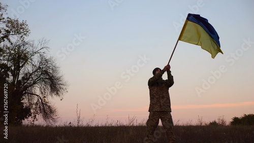 Cuadro en lienzo Male military waving blue-yellow banner on liberated territory occupied by russia