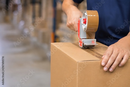 Person sealing a cardboard box with tape dispenser