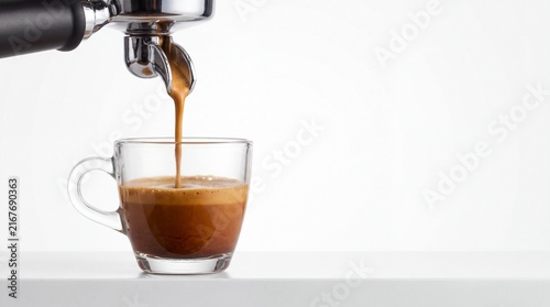 Fresh espresso pouring into clear glass cup from stainless steel portafilter for rich coffee brewing