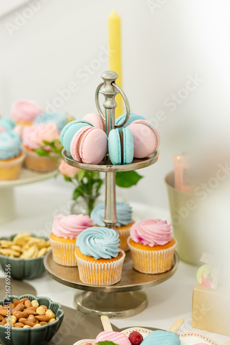 Cuadro en lienzo Sweet Delights Display: A tiered stand laden with pastel-colored cupcakes and macarons, accompanied by bowls of nuts and a solitary candle, creates an inviting dessert table setup for a celebration