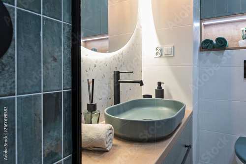 Modern bathroom sink with tap and round mirror on the tiled wall. Stylish interior of bath room in hotel room. Real estate.