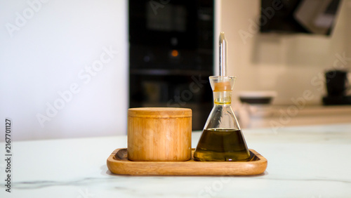A glass bottle of olive oil with a wooden salt box. Blurred background.