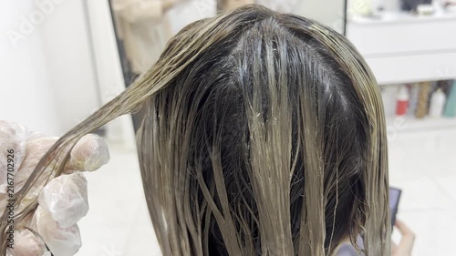 Hairdresser hand holding hair strand applying dye close up 16:9, beauty salon concept