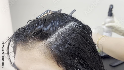 Hairdresser applying scalp treatment serum to woman hair roots close up 16:9, beauty salon concept
