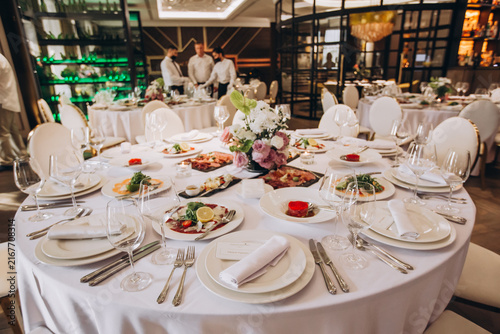 Bild auf Leinwand Elegant Dining Setup: A round dining table adorned with fine white linen, set with complete tableware, elegant glassware, and a beautiful floral centerpiece