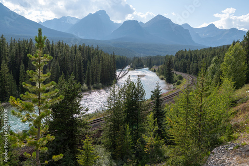 Morant's Curve in Banff National Park, Canada, with the Bow River winding through dense forest beneath the dramatic Canadian Rocky Mountains on a scenic summer day.