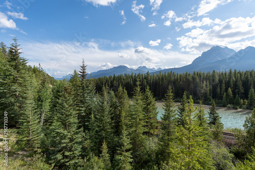 Morant's Curve in Banff National Park, Canada, with the Bow River winding through dense forest beneath the dramatic Canadian Rocky Mountains on a scenic summer day.