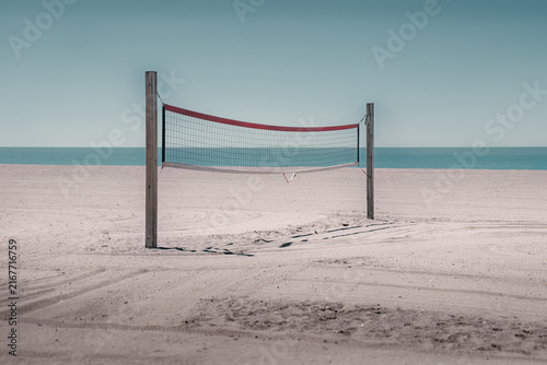 Fotografie Empty beach volleyball net on sandy beach beside calm water
