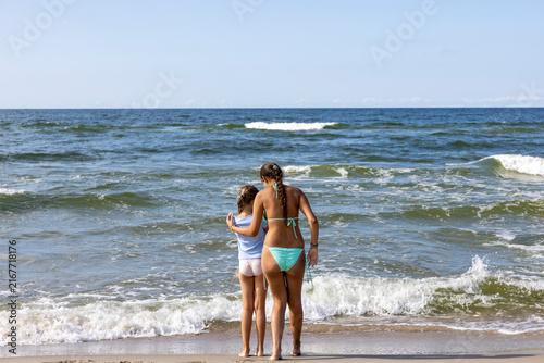 Two Girls Standing Together Watching Ocean Waves at Beach